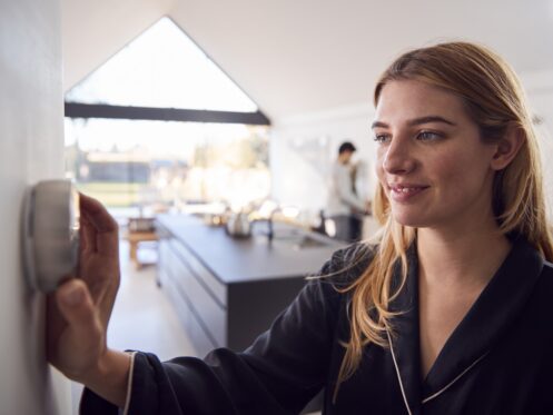 Woman Adjusting Wall Mounted Digital Central Heating Thermostat Control At Home